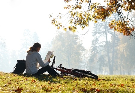 woman cyclist with read the map sitting on halt illuminated by the rays of bright sunlight among the green nature
